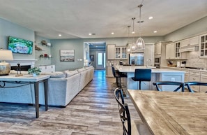 A spacious kitchen with modern appliances, a dining area with a wooden table, and a living room with a sofa and TV. - Ocean View * 5BR Luxury Single Family House! (Ocean View)