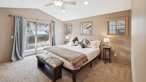 A bedroom with a large bed, a bench, a ceiling fan, and a view of the outdoors through a sliding door.