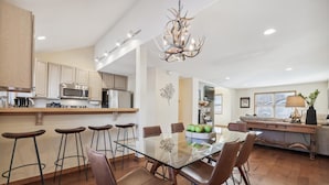 A modern kitchen with a central island, bar stools, and a dining table with chairs.