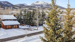 A cabin with a snow-covered roof, surrounded by evergreen trees and a mountain in the background.