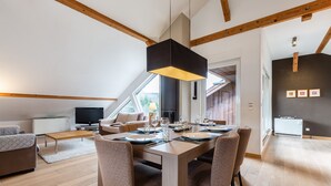 Un coin repas avec une table en bois dressée pour quatre personnes, entourée de chaises en osier, sous un luminaire suspendu.