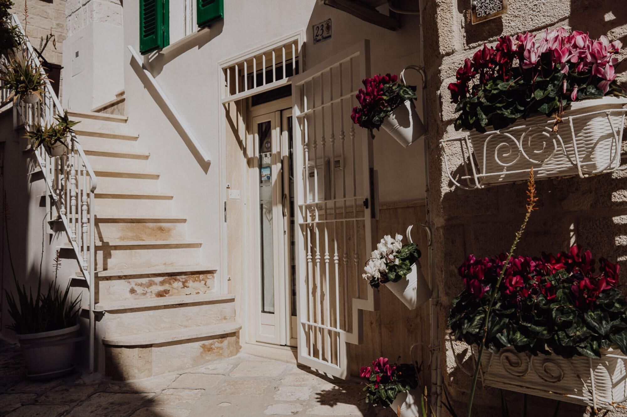 A narrow street with a white building, a staircase, and balconies with flowers.