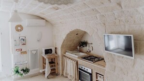 A kitchen with a stone arch, a stove, a microwave, and a TV mounted on the wall. - Casa Vacanze Portanuova Monopoli (Monopoli)