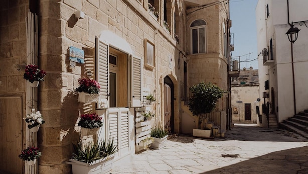 A narrow street with stone buildings, shutters, and potted plants. - Casa Vacanze Portanuova Monopoli (Monopoli)