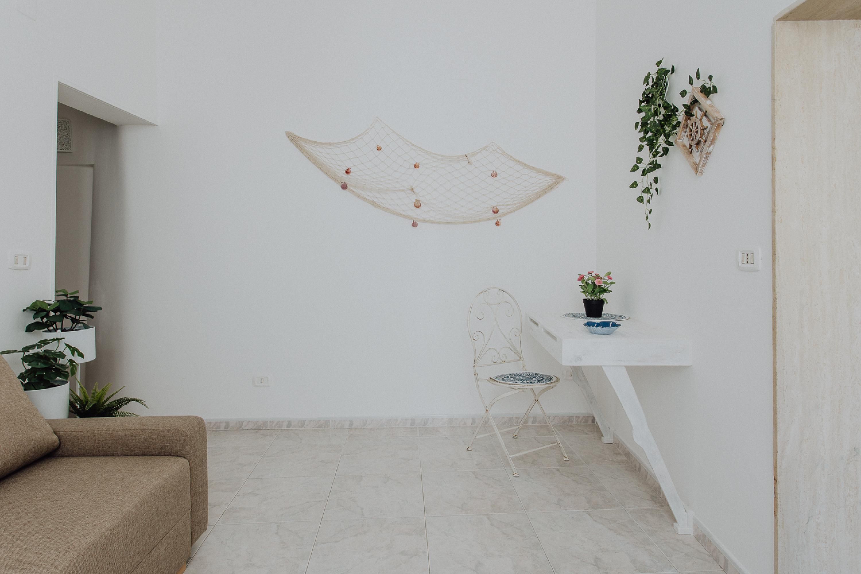 Ein minimalistisch eingerichtetes Wohnzimmer mit einer Couch, einem Wandteppich, einem kleinen Tisch mit Topfpflanze und einem Sessel.