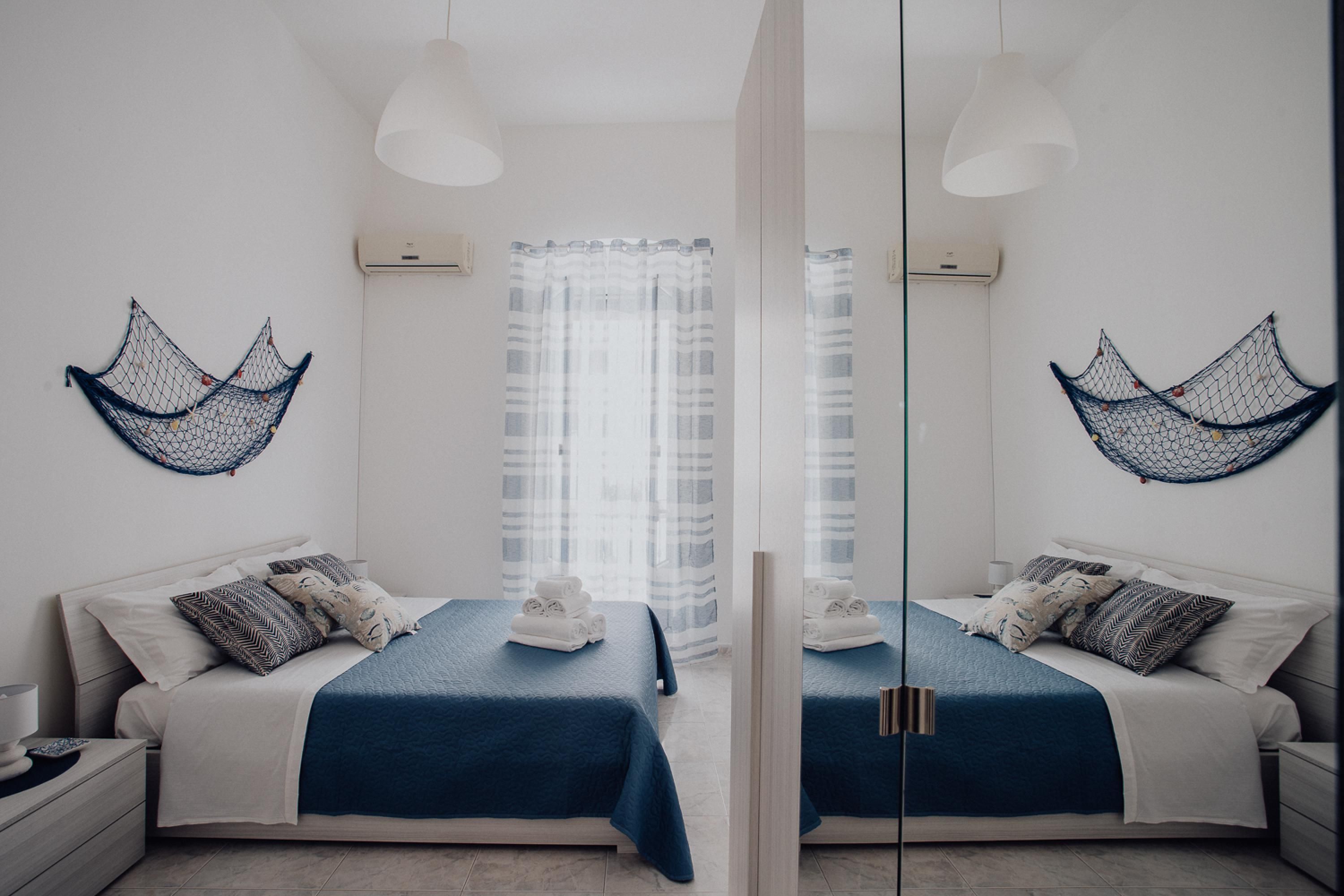 A mirrored room with two beds, white bedding, blue accents, and decorative net wall hangings.