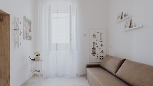 A minimalist room with a white door, a small table with a vase, a beige sofa, and wall-mounted shelves with decorative items. - La Dimora di Stesa in Monopoli (Monopoli)
