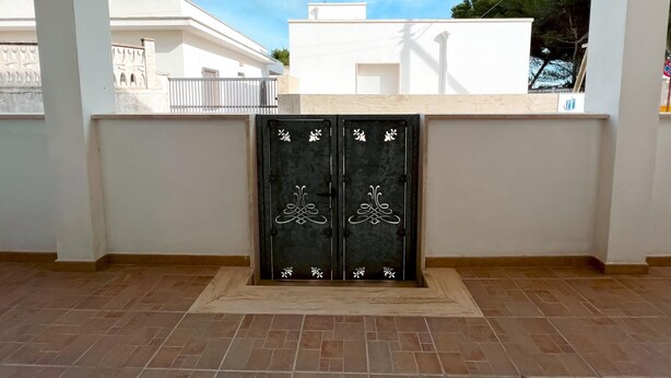 A room with a tiled floor, a white wall, and a black door with decorative white patterns. - Appartamento 69 in Casalabate (Squinzano)