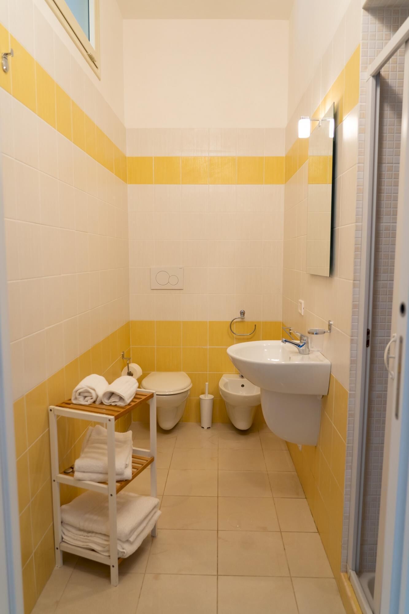 Een kleine badkamer met gele en witte tegels, een wastafel, toilet, douchetoilet en een handdoekhouder.