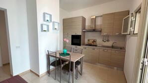 A modern kitchen with light wood cabinets, a built-in oven, and a dining area with a table and chairs. - Appartamento 69 in Casalabate (Squinzano)