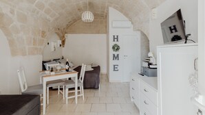 Une pièce chaleureuse avec un plafond en pierre, un lit doté d’une tête de lit grise, une commode blanche et un bureau avec des chaises.