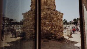 Une structure en pierre à la texture rugueuse, peut-être un monument historique, entourée d’une zone pavée où des personnes se promènent.