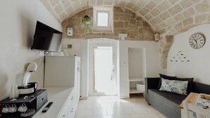 Un salon moderne avec un plafond en pierre, un téléviseur à écran plat, une machine à café, un canapé agrémenté de coussins décoratifs et une horloge murale.