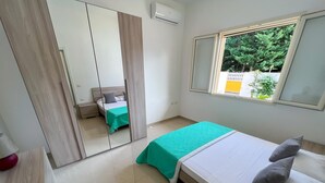 A bedroom with a bed, a window with a view of greenery, a mirror, and a wardrobe. - Appartamento 73 in Casalabate (Squinzano)