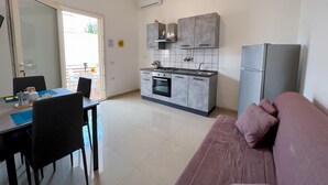 A compact kitchen with a stove, sink, and modern cabinetry. There is a dining area with a table and chairs, and a sofa in the living area. - Appartamento 73 in Casalabate (Squinzano)