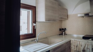 A kitchen with a double sink, wooden cabinets, a window, and a tiled backsplash. - Dimora Silvia in Monopoli (Monopoli)