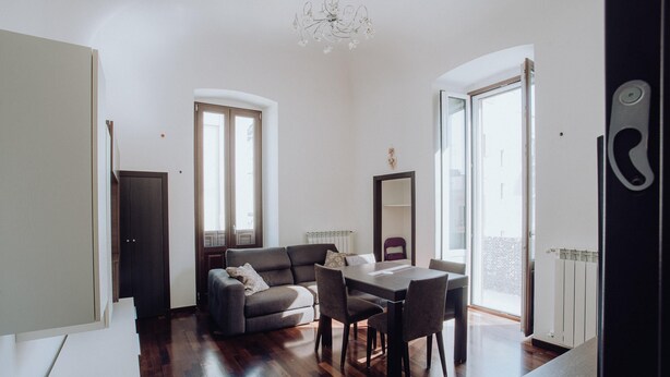 A modern living room with a sofa, dining table, and chairs. There are large windows and a chandelier. - Dimora Silvia in Monopoli (Monopoli)