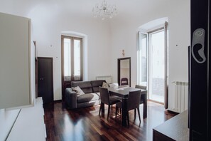 A modern living room with a sofa, dining table, and chairs. There are large windows and a chandelier. - Dimora Silvia in Monopoli (Monopoli)