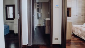 A hallway leading to a bathroom with a toilet, sink, and towel rack. There is a bed with a patterned bedspread on the right and a blue bed in the left room. - Dimora Silvia in Monopoli (Monopoli)