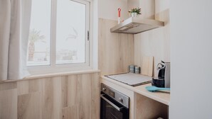 A compact kitchen with a window, wooden paneling, a built-in oven, and a coffee maker. - Casa Azzurra in Capitolo (Monopoli)