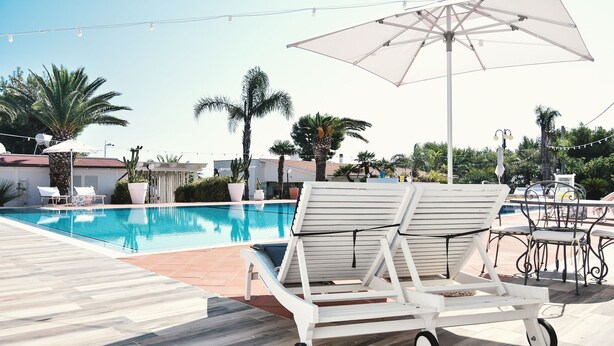 A poolside area with a clear blue pool, lounge chairs, and a pergola with an umbrella. - Casa Azzurra in Capitolo (Monopoli)