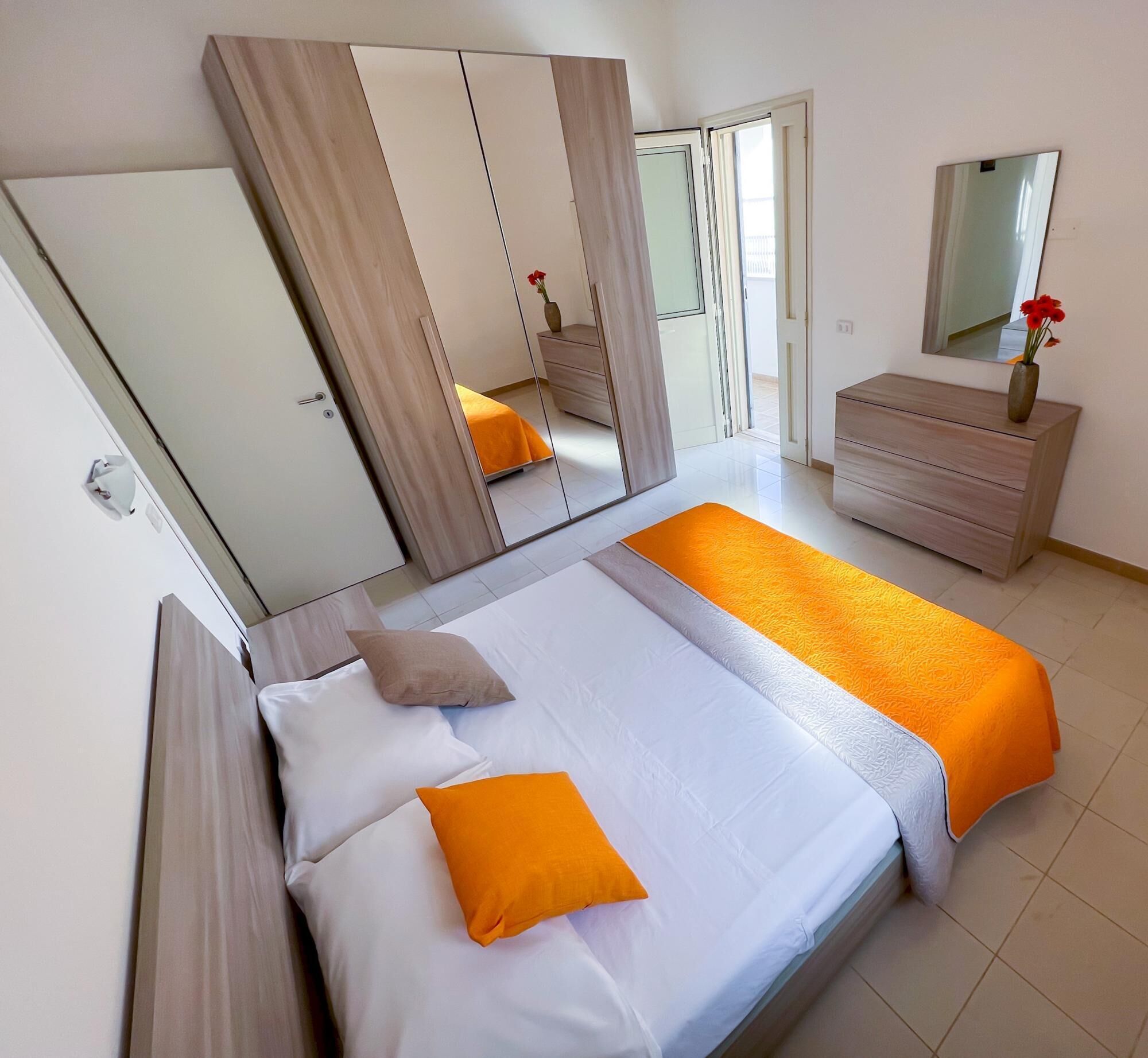 Quarto com uma cama, penteadeira, espelho e porta.