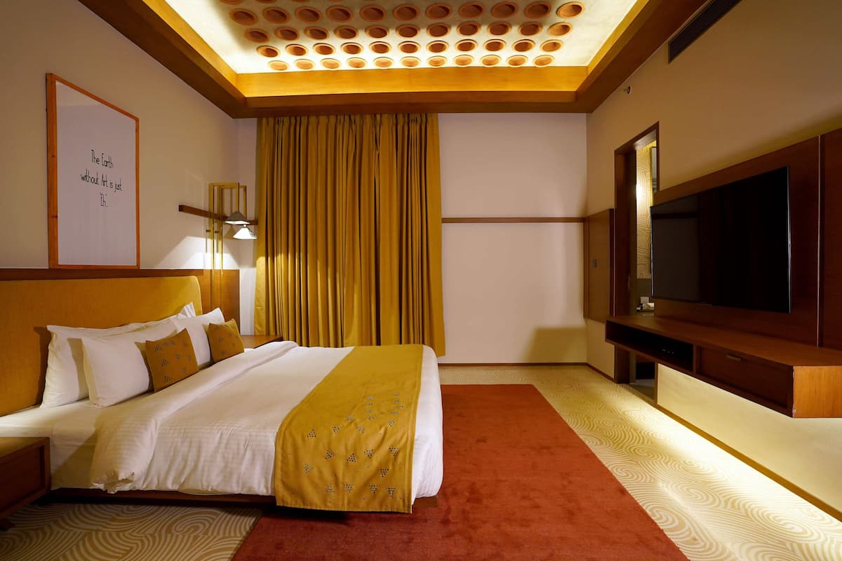 A hotel room with a large bed, a flat-screen TV, a ceiling with circular patterns, and a framed quote on the wall.