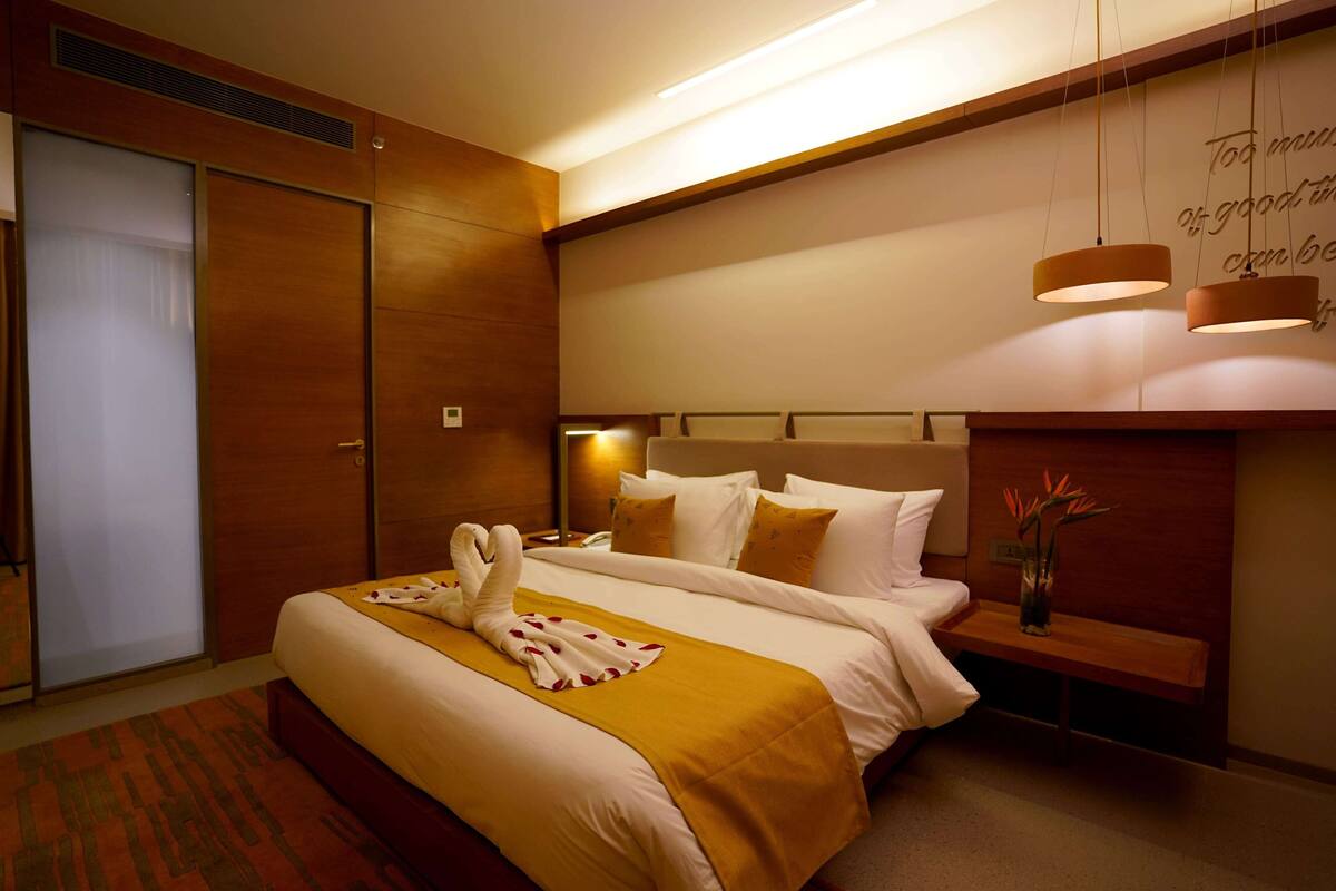 A hotel room with a large bed, a bedside table with a vase, and a wall-mounted light fixture.