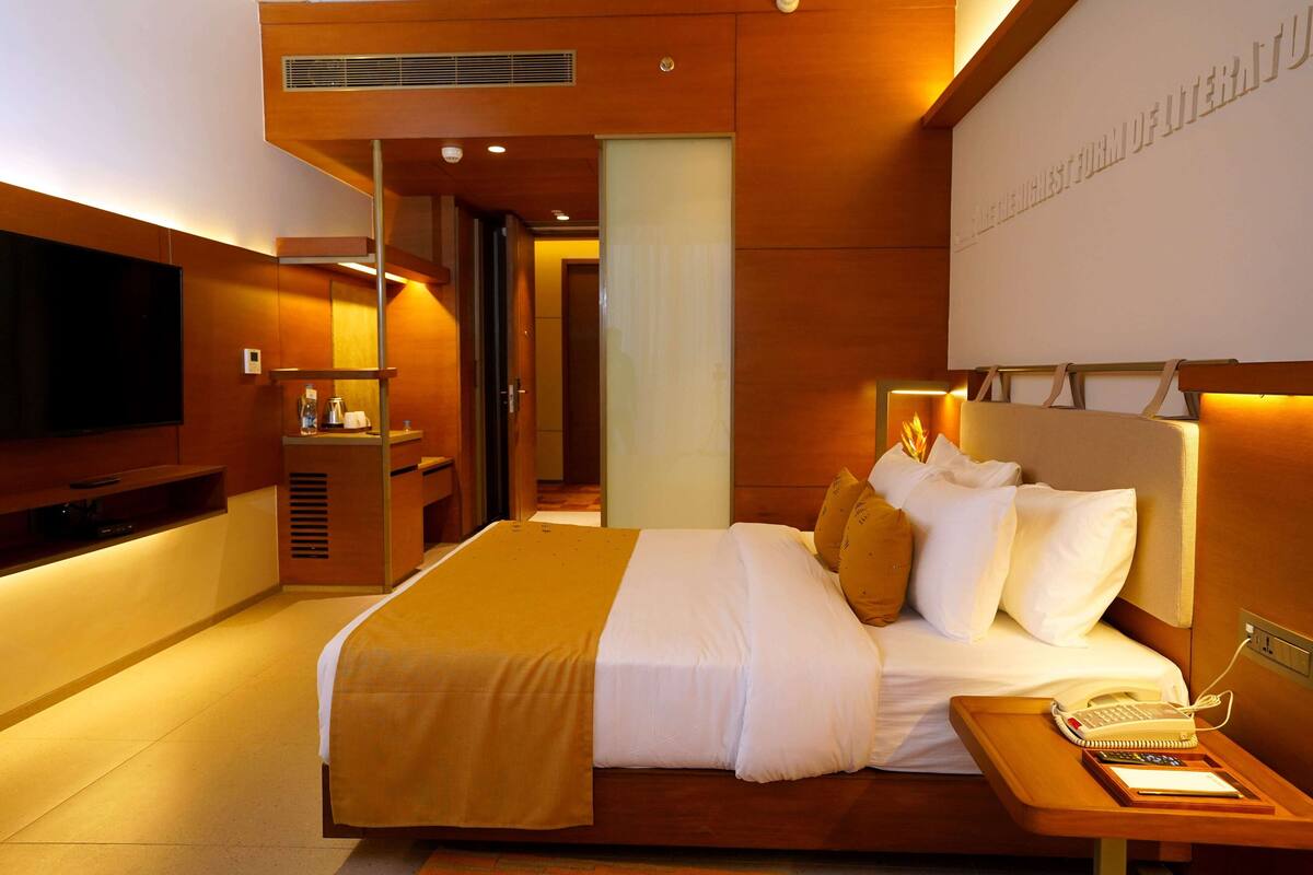 A modern hotel room with a large bed, a bedside table with a phone and a book, and a TV mounted on the wall.