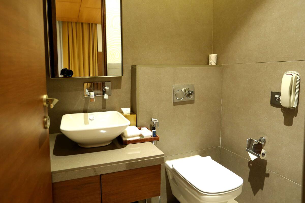 A modern bathroom with a sink, mirror, toilet, and a hairdryer mounted on the wall.