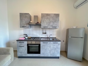 A modern kitchen with grey cabinets, a built-in oven, a stainless steel sink, and a refrigerator.