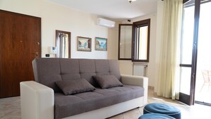 A living room with a grey sofa, two blue ottomans, a wooden door, and a window with a curtain. - Elle Dimore in Lecce (Lecce)