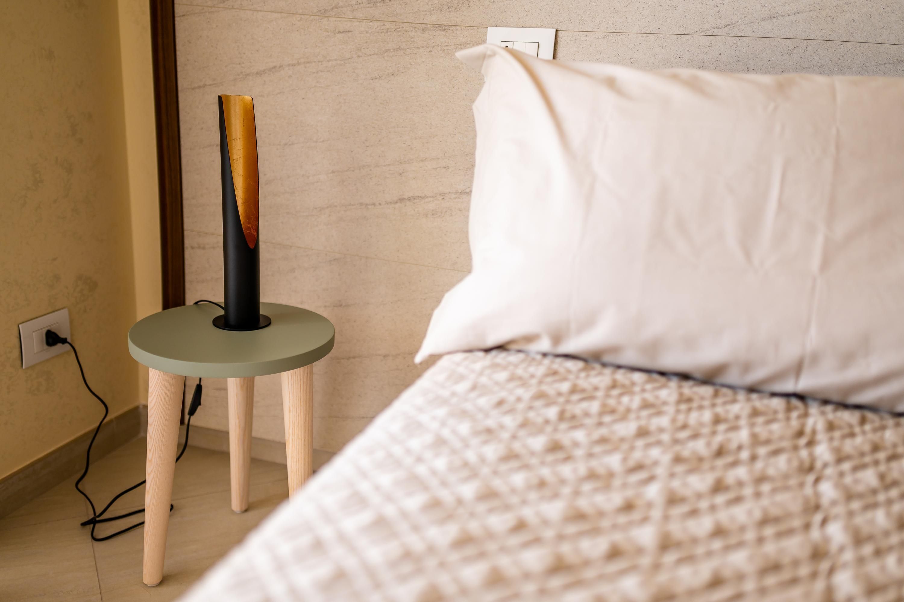 A bedroom with a bed, a bedside table with a lamp, and a power outlet on the wall.