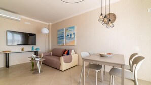A modern living room with a sofa, dining table, and chairs, a flat-screen TV, and artwork on the wall. - La Stella sul Mare in Monopoli (Monopoli)