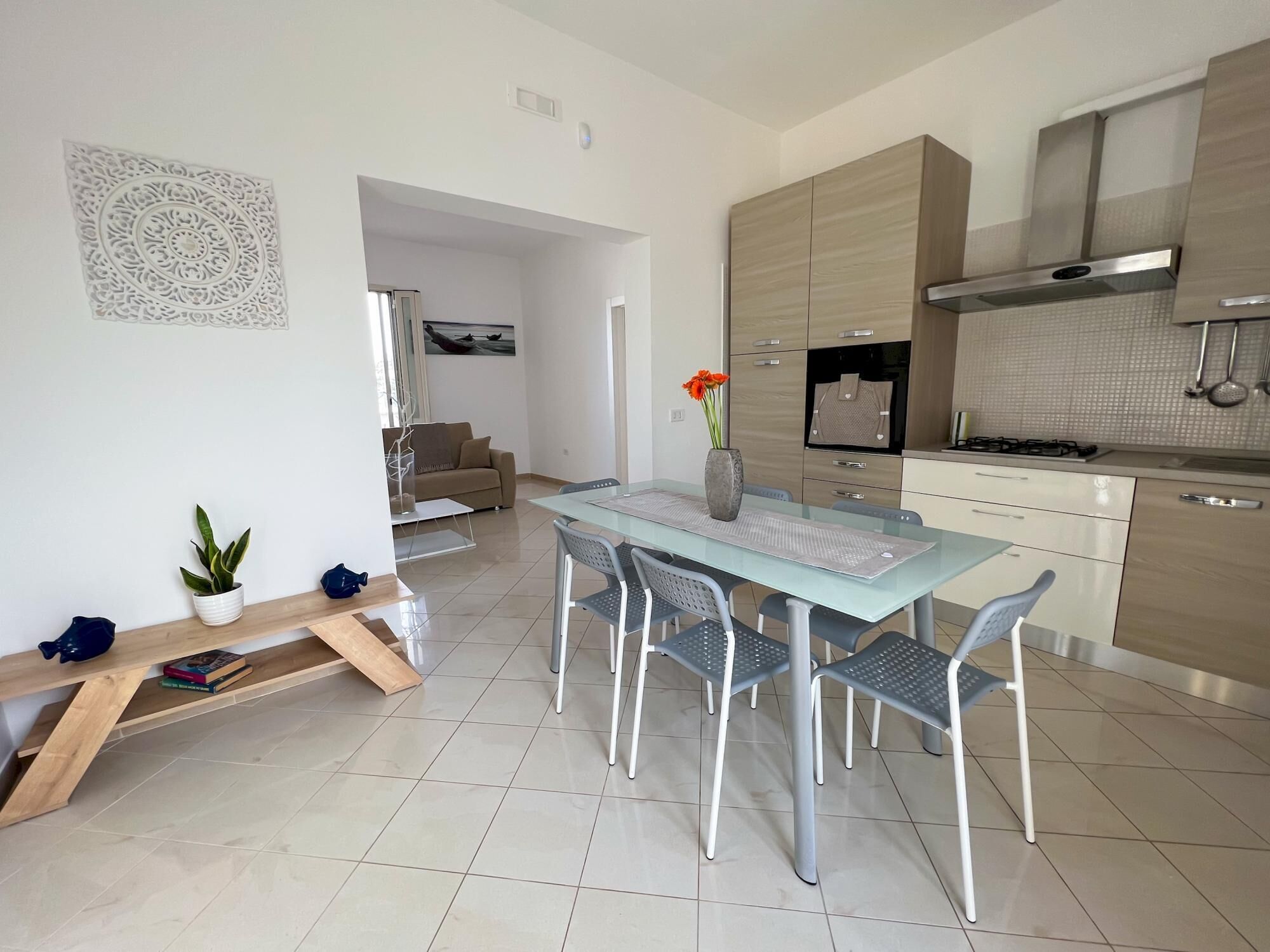 A modern kitchen with a dining area, featuring a glass table, metal chairs, and a built-in oven.