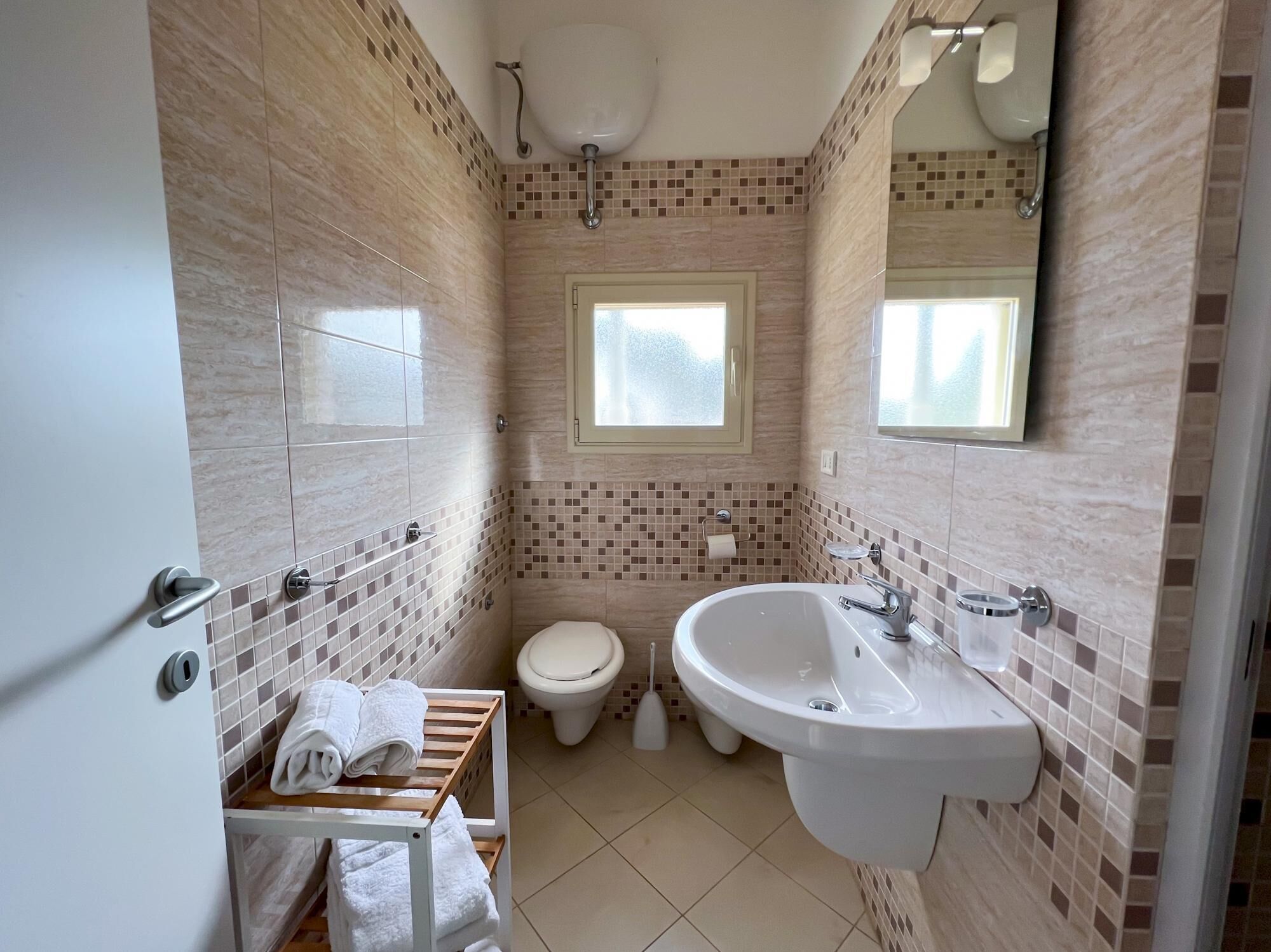 Een badkamer met toilet, wastafel en een raam.