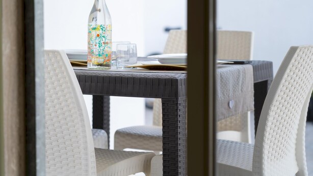Een eetgedeelte met rieten stoelen en een tafel voor twee personen, met een glazen fles met kleurrijke patronen en een glas.
