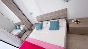 Een moderne hotelkamer met een groot bed, twee kussens, een nachtkastje, een boek en een spiegel.