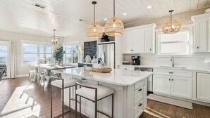 A modern kitchen with white cabinetry, a large island with bar stools, pendant lights, and a view to the outside. - Pet-Friendly Beach House w/ Heated Pool (Port St. Joe)