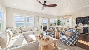 A spacious living room with a large sofa, a coffee table, and two patterned armchairs. There are large windows offering a view of the ocean. - Pet-Friendly Beach House w/ Heated Pool (Port St. Joe)