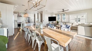 A spacious kitchen with a wooden dining table and white chairs, a large pendant light, and a TV mounted on the wall. - Pet-Friendly Beach House w/ Heated Pool (Port St. Joe)