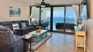 Sala de estar com sofá, mesa de centro e vista para o oceano através de grandes portas de vidro.