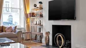 Un salon comprenant un canapé, une table basse, un téléviseur fixé au mur, une cheminée et une fenêtre avec des rideaux.
