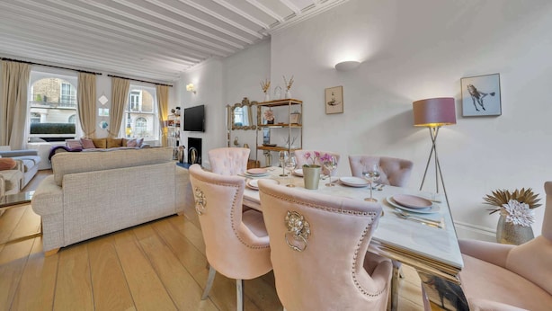 Un salon bien éclairé, avec un canapé, une table à manger et des chaises. On y trouve également un téléviseur, une bibliothèque et une lampe.