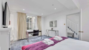 Une chambre d’hôtel comprenant un lit, un bureau, une chaise, une télévision, une fenêtre avec des rideaux, un miroir et un escalier.