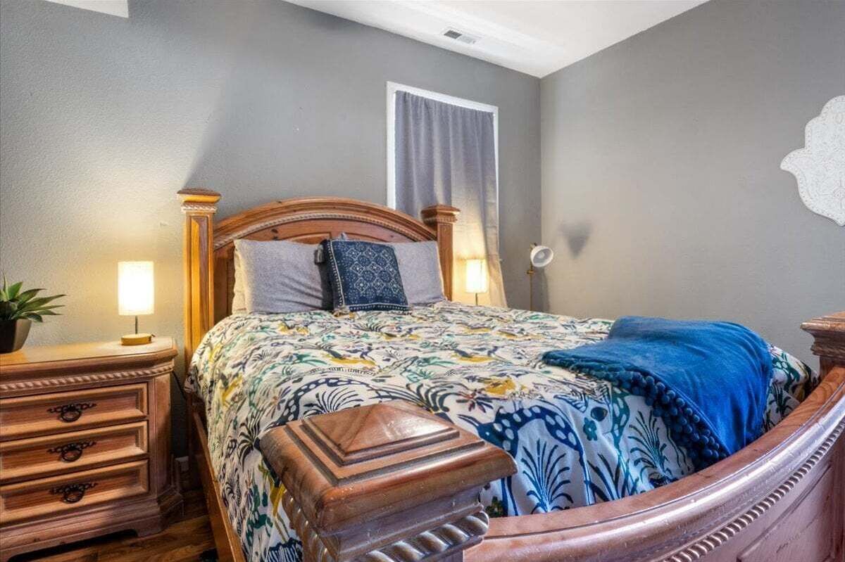 Quarto com cama de madeira, mesa de cabeceira, abajur e janela com cortinas.