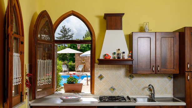 A kitchen with wooden cabinets, a gas stove, and a view of an outdoor swimming pool. - Il Ciliegio ,'le Calme et la Tranquillité Sont Notre Carte de Visite' (Castelbuono)
