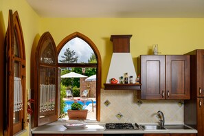A kitchen with wooden cabinets, a gas stove, and a view of an outdoor swimming pool. - Il Ciliegio ,'le Calme et la Tranquillité Sont Notre Carte de Visite' (Castelbuono)