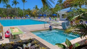 A swimming pool with lounge chairs and umbrellas, surrounded by palm trees and a covered area. - Florida Keys Getaway - Slps 4 -  Ocean View (Tavernier)