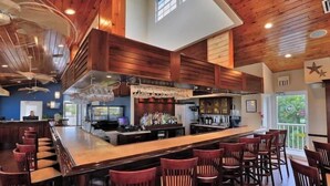A bar area with a high ceiling and wooden paneling, featuring a long counter and multiple bar stools. - Toes in the Sand - 2 Bedroom Condo Sleeps 4 (Tavernier)